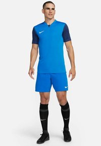 Maillot bleu avec manches marine, shorts bleus assortis, chaussettes noires et chaussures noires. Présente le logo Nike sur la poitrine et les chaussettes.