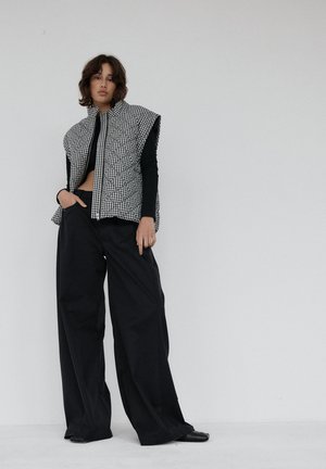 Pikowana kamizelka w czarno-białą krateczkę z kołnierzykiem na stojaku, zestawiona z wysokim stanem czarnymi spodniami o szerokich nogawkach, noszona na czarnym topie.