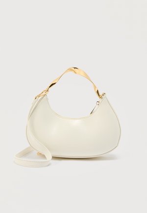 Krémová kabelka ve tvaru půlměsíce s lesklým zlatým krátkým uchytem a odpovídajícím dlouhým popruhem na jednobarevném světlém pozadí.