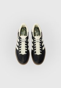 Črni in krem športni čevlji s tremi črtastimi poudarki, teksturirano mrežico in sintetičnim zgornjim delom, okrogel prst in rjavim gumijastim podplatom.