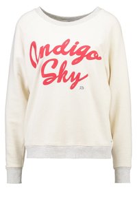 Sweatshirt crème avec texte rouge « Indigo Sky », accents gris sur l'encolure et les poignets, tissu doux, coupe décontractée, ourlet côtelé.