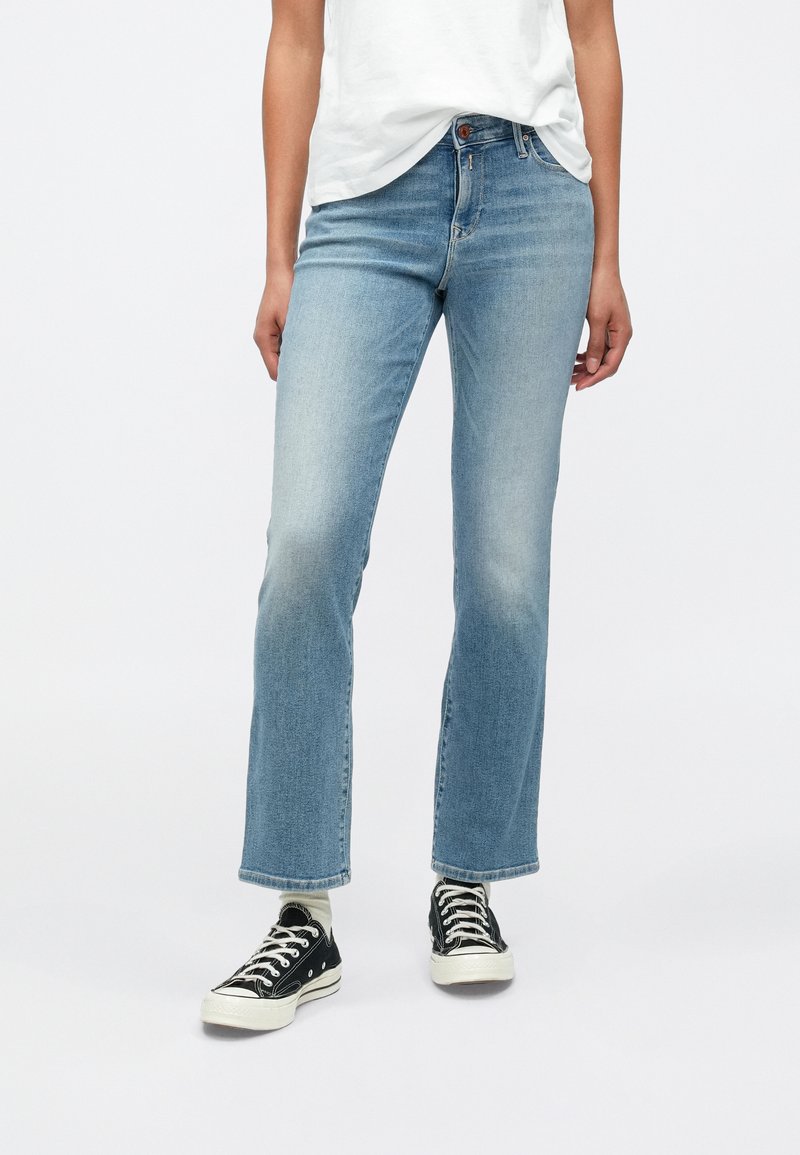 Ανοιχτό μπλε τζιν παντελόνι με φαρδιά μπατζάκια και ξεθωριασμένο φινίρισμα, με κούμπωμα κουμπιού και πίσω τσέπες, συνδυασμένο με μαύρα αθλητικά παπούτσια.