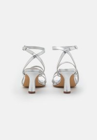 Srebrne sandały na wysokim obcasie z paskami, z krzyżującym się designem pasków, skromnym obcasem i teksturowanym metalicznym wykończeniem.