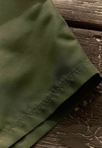 Olive-zöld szövet sima textúrával, tiszta szegéllyel és varrott részletekkel. Az anyag könnyűnek és tartósnak tűnik.