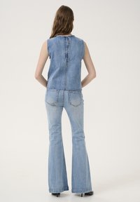 Denim majica bez rukava i ravne traperice svijetloplave boje. Majica ima šav na sredini leđa; traperice imaju klasične zadnje džepove s detaljima šivanja.