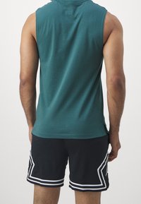 Top sin mangas verde con escote redondo, combinado con pantalones cortos negros perforados que presentan acentos laterales blancos y un patrón geométrico.