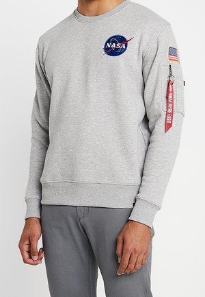 Szara bluza z logo NASA na piersi, naszywką amerykańskiej flagi na rękawie oraz czerwoną metką "Remove Before Flight" zwisającą z zamka.