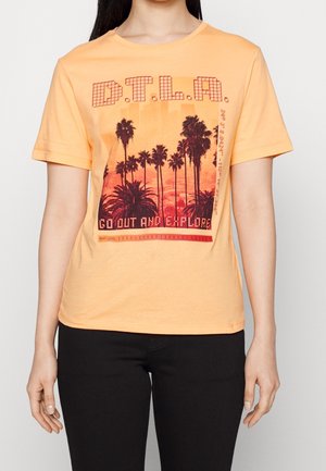 Femme portant un T-shirt pêche avec un graphisme de palmiers au coucher du soleil et le texte "D.T.L.A." et "Sortez et explorez."