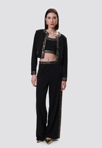 Zwarte tweedelige outfit met een cropped jack en hoge taillebroek, beide versierd met metallic accenten en geometrische patronen.