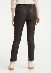 Černé, přiléhavé džíny s lesklou texturou, designem se pěti kapsami a hnědou koženou nášivkou na pase. Konec nohavic je uprostřed kotníku.