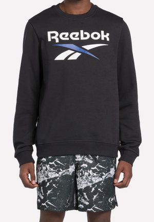 Person iført en sort Reebok sweatshirt med hvidt og blåt logo og sort-hvide marmorerede træningsshorts.