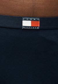 Gros plan sur un tissu marine avec un petit patch logo rectangulaire Tommy Hilfiger présentant un bloc de couleurs blanc et rouge.