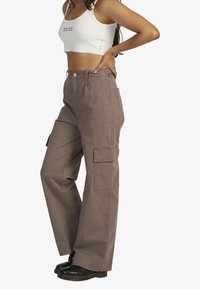 Cargo pants made of lightweight cotton in a taupe color, featuring wide legs, large side pockets, and a button closure at the waist.