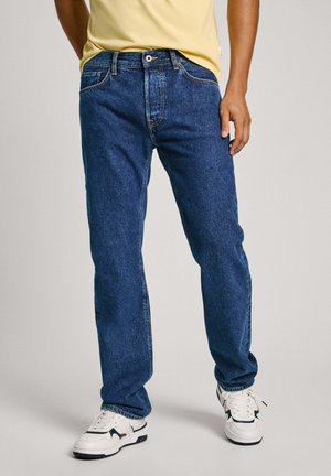 Blauwe denim jeans met een klassiek recht model, vijf zakken, contrasterende stiksels en een versleten look, gecombineerd met witte sneakers.