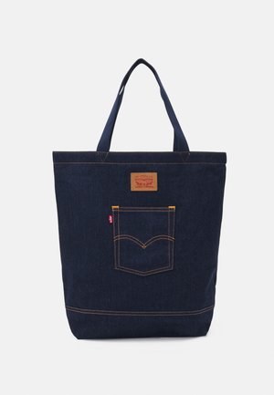 Mørkeblå denimshopper med to håndtag, forlommer med syning og et lille brunt lædermærke nær toppen midt på.