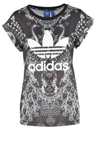 Svart och vit Adidas t-shirt med stort logotyp, som har intrikata symmetriska påfågelvinge- och ornamentala mönster.