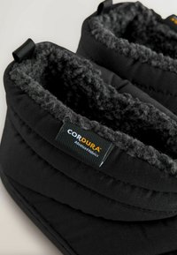 Papuci negri cu căptușeală moale și pufoasă. Realizați dintr-un material durabil Cordura, cu un exterior texturat și detalii din material textil.