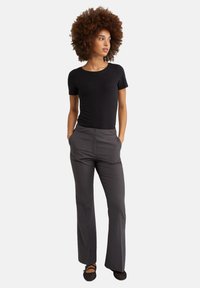 Top corto nero a maniche corte abbinato a pantaloni grigi su misura. I pantaloni presentano una parte anteriore piatta e una linea dritta. Scarpe nere in rete completano il look.