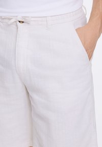 Linen shorts in light beige with a textured, slightly crinkled finish. Features front pockets and a casual drawstring waistband.