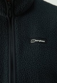Čierna fleecová bunda s textúrovaným povrchom, so zipsom po celej dĺžke a malým bielym logom Berghaus na hrudi.