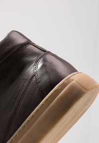 Bottine en cuir marron avec une texture lisse, dotée de détails cousus et d'une semelle en caoutchouc beige avec un fond texturé.