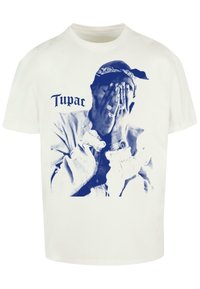 Hvid t-shirt med et blåt grafisk tryk af en person, der dækker sit ansigt med hænderne. "Tupac" er trykt i en dekorativ skrift ovenfor.