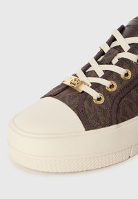 Pruunimustriline lõuendist toss valge kummist varbakatte, kuldsete detailide ja kreemjate paeltega. Tekstuuriga külgpaneelid täiustavad disaini.