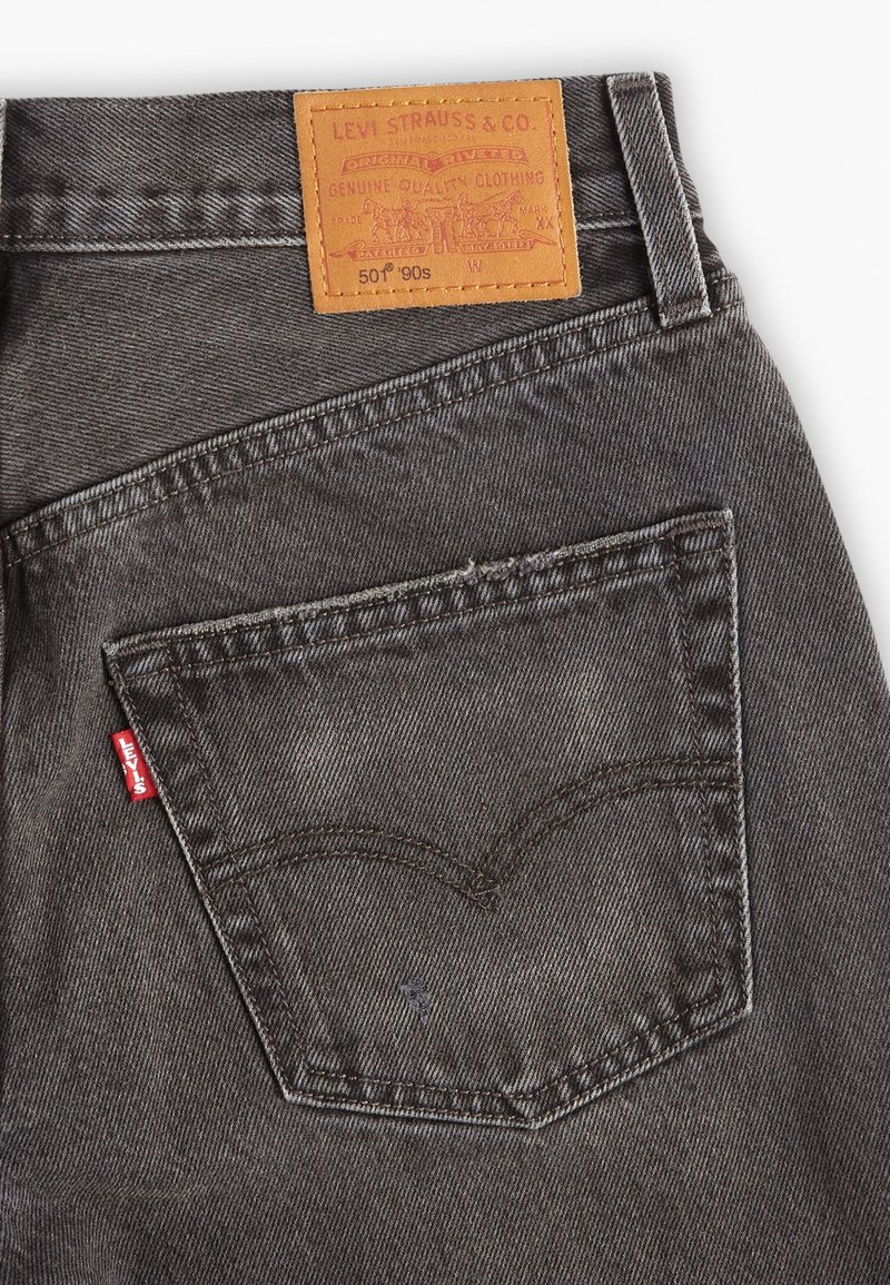 Jean en denim gris foncé avec une patch en cuir marron portant l'inscription "LEVI STRAUSS & CO." et une étiquette rouge sur la poche arrière gauche. Présente un couturage classique.
