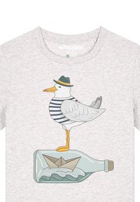 Das graue T-Shirt zeigt eine Möwe in einem gestreiften Hemd und einem grünen Hut, die auf einer Flasche steht, neben einem gefalteten Papierboot und einem Wellenmotiv.