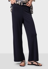 Breda navybyxor tillverkade av ett mjukt, elastiskt material. Har en hög midja och är kombinerade med svarta platta sandaler.