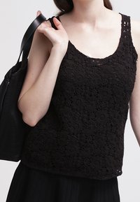 Top negro de encaje con un patrón floral, escote redondo y tirantes anchos, combinado con un bolso negro.