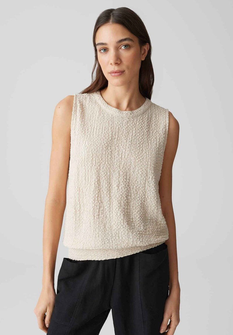 Top senza maniche beige chiaro, tessuto con trama, scollatura rotonda e fondo orlato. Design minimalista, texture morbida, adatto per un abbigliamento casual.