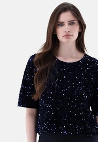 Marineblaues Paillettenoberteil mit kurzen Ärmeln, das über einen runden Ausschnitt verfügt und eine strukturierte Oberfläche aufweist, die durch verstreute schimmernde Pailletten entsteht.