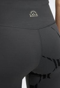 Κοντινή λήψη μαύρων κολάν με ψηλή μέση, λογότυπο «LALA BERLIN» και διακριτή ραφή με μοτίβο στην περιοχή του ισχίου και του μηρού.