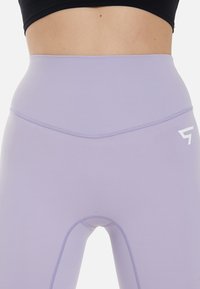 Visoko pasovi leggingi iz svetlo sivkaste tkanine. Imajo eleganten, brezšiven dizajn in kontrastno belo logotipno podrobnost na bokih. Raztegljiv material.