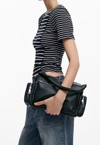 Zwarte leren handtas met een gestructureerde afwerking, omvlochten handvat en meerdere met rits afgesloten compartimenten. Gecombineerd met een gestreepte top en denim.