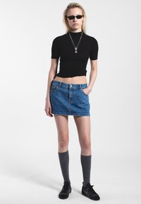 Top corto nero a maniche corte, mini gonna di jeans blu, calze grigie fino al ginocchio e scarpe da ginnastica nere. Gli accessori includono collane in argento a più strati.