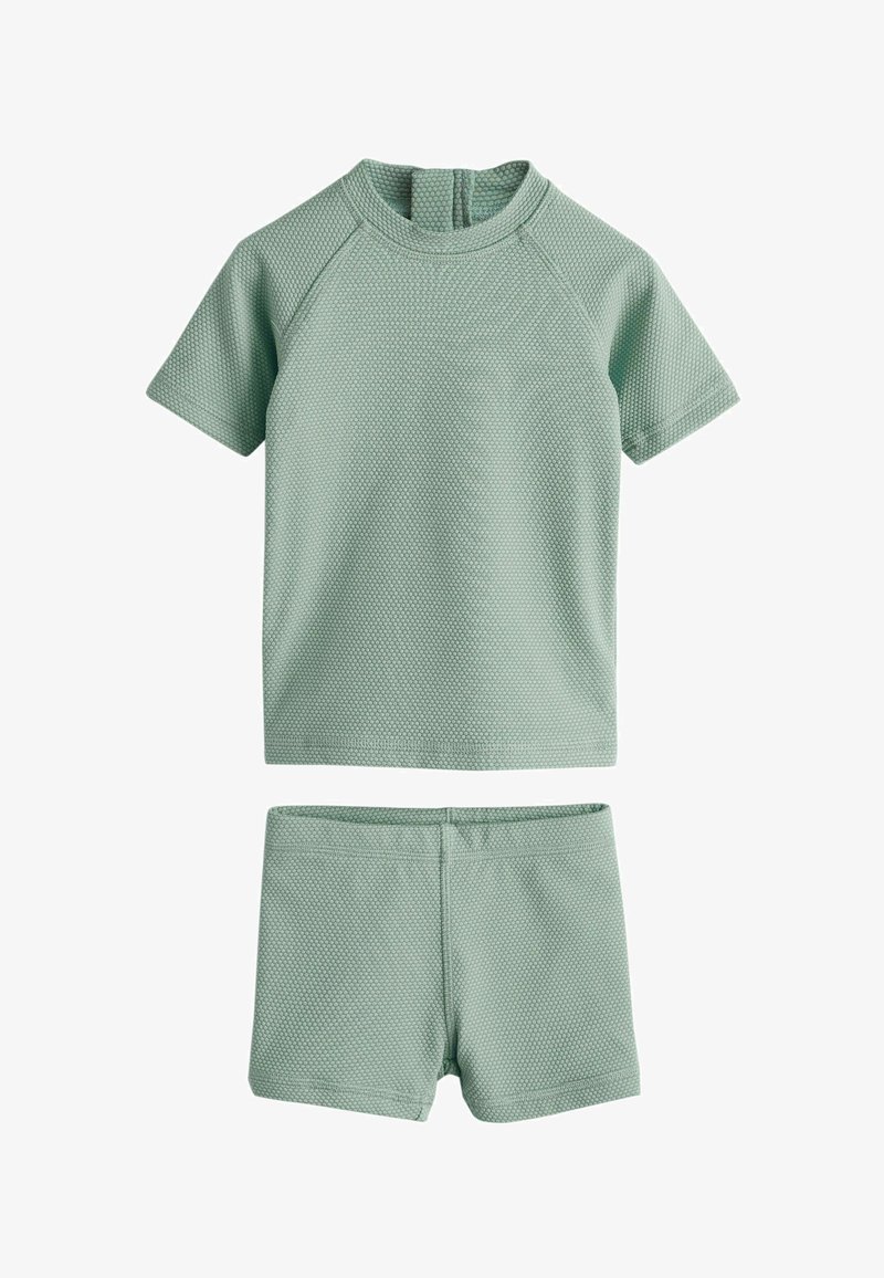 Haut à manches courtes vert clair texturé avec col rond et short assorti. Le tissu présente un motif de points en relief. Design minimaliste.