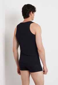 Schwarzes Tanktop mit gerippter Textur, tailliertem Design und weiten Armausschnitten, kombiniert mit passenden schwarzen Boxershorts und einem einfachen Silhouette.
