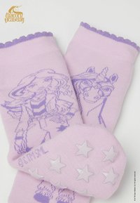 Różowe skarpety z jednorożcem i postacią w jaśniejszym odcieniu fioletu, z falbanką na górze oraz gwiazdkowymi, antypoślizgowymi gripami na spodzie.