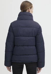 Námořnická puffer bunda s vysokým límcem a prošívanými blokovými panely. Disponuje hladkou texturou a širokými, zateplenými rukávy pro teplo.