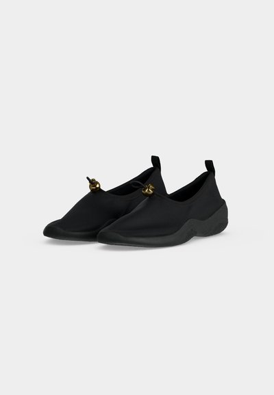 Ζευγάρι μαύρα παπούτσια τύπου slip-on με στρογγυλεμένες μύτες και ρυθμιζόμενα κορδόνια με κλιπ, σε λευκό φόντο.