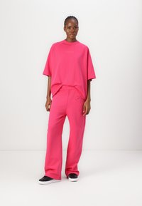 Rosa oversized t-skjorte med kort erm og logo, sammen med matchende vide bukser laget av mykt stoff. Svarte treningssko fullfører antrekket.