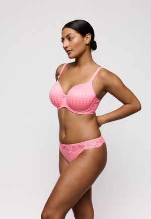 Vrouw met donker haar in een lage knot, gekleed in een roze geruit beha en slipjes met kanten rand, staand met haar handen achter haar rug tegen een effen achtergrond.