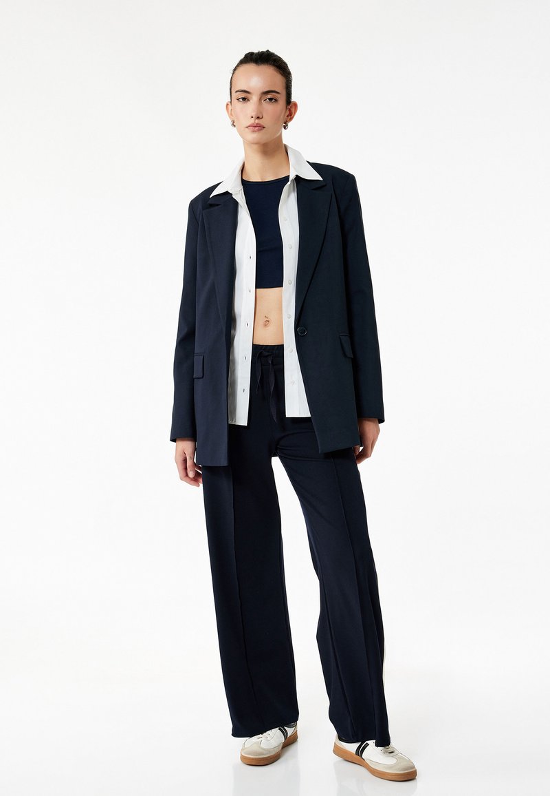 Marineblå skræddersyet blazer med hvid skjorte og marineblå crop top, parret med løse marineblå bukser og afslappede sneakers.