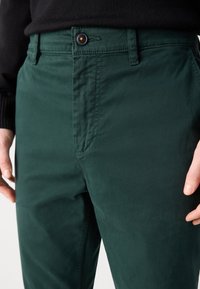 Chinos de algodón verde con una textura suave, que presentan un cierre de botón, bolsillos laterales y un diseño de pierna recta.