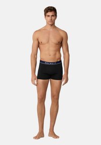 Boxer briefs neri in cotone con una vita blu navy etichettata "HACKETT." Il tessuto appare liscio e aderente, progettato per una vestibilità a contatto con il corpo.