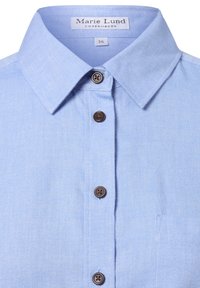 Light blue button-up shirt with a pointed collar, featuring a textured fabric, brown buttons, and a chest pocket on the left side.