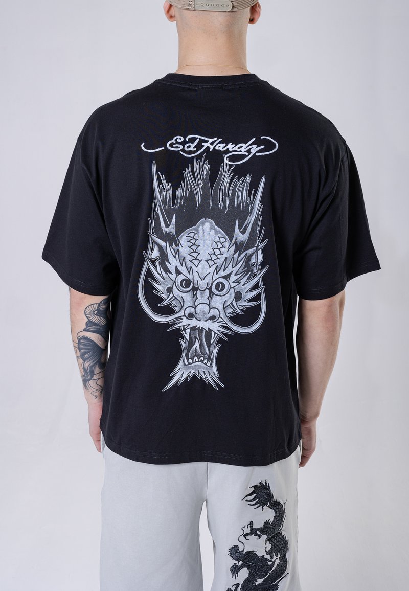 Black cotton t-shirt featuring a large silver dragon graphic on the back, with the text "Ed Hardy" above. Relaxed fit and short sleeves.