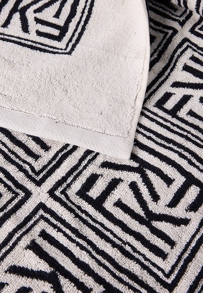 Λευκή και μαύρη πετσέτα με γεωμετρικό μοτίβο διπλωμένη πάνω σε άλλη πετσέτα με τον ίδιο σχεδιασμό και υφή.